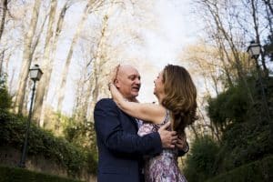 En el corazón de un bosque iluminado por el sol, una pareja se abraza tiernamente entre árboles y farolas antiguas, encapsulando la esencia de los encantadores paisajes de "Un paseo de fotografía en pareja en Granada". - ForTwo - Planes para parejas