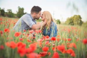 Una pareja en un mar de flores rojas, sentada cerca y sonriendo, captura a la perfección la esencia de Session Love. Este momento es un adelanto de su historia, extraído del libro "Libro de fotografía para parejas: Session Love". - ForTwo - Planes para parejas