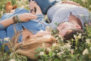 Una pareja yace sobre el césped, sonriendo entre flores silvestres en un día soleado, capturando el amor en cada mirada: una fotografía perfecta para "Libro de fotografía para parejas: Session Love" para atesorar momentos juntos. - ForTwo - Planes para parejas