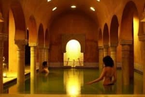 Dos personas se relajan en el MIDRA de Hammam Al Ándalus Granada, una piscina cubierta que evoca un hammam clásico granadino con techos abovedados e iluminación cálida que crea un ambiente sereno. - ForTwo - Planes para parejas