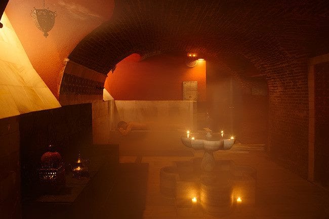 Experimente un ambiente cálido en Hammam Al Ándalus Madrid con “Baño y masaje individual MIMMA 30”, con una iluminación tenue y acogedora, techos de ladrillo arqueados, velas y una fuente central de mármol. - ForTwo - Planes para parejas