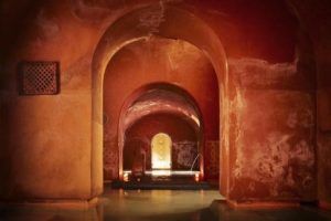 La Oferta Baño árabe con masaje en Hammam Al Ándalus Madrid ofrece un ambiente tranquilo con puertas arqueadas e iluminación cálida que se refleja en el suelo de agua, evocando un antiguo balneario. Experimente una serenidad sin igual. - ForTwo - Planes para parejas
