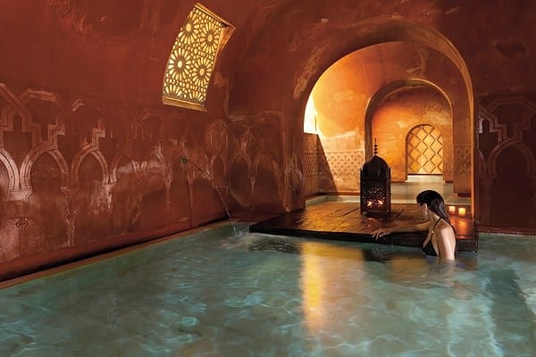 Relajarse en una piscina cubierta adornada con arcos y ventanas intrincadas, que recuerda una experiencia serena en la Oferta Baño árabe con masaje de Hammam Al Ándalus Madrid. - ForTwo - Planes para parejas
