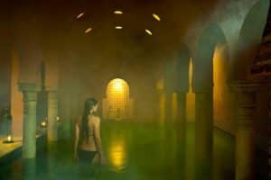 En una piscina cubierta oscura y atmosférica similar a MIDRA por Hammam Al Ándalus Granada, los arcos y la iluminación suave crean un ambiente sereno para una verdadera tranquilidad. - ForTwo - Planes para parejas