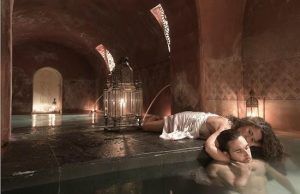 Dos personas se relajan entre los tonos cálidos y la suave iluminación de las arcadas del spa Hammam Al Ándalus de Madrid mediante elegantes faroles, disfrutando de la relajante experiencia de Baño y Masaje individual MIDRA 30. - ForTwo - Planes para parejas