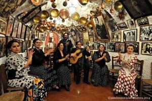 Un espectáculo de flamenco en la zambra María la Canastera cautiva con los intérpretes, los bailarines aplaudiendo y el guitarrista situado en el centro de una sala ricamente decorada. - ForTwo - Planes para parejas