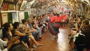 En una sala estrecha y abarrotada, una bailaora de flamenco vestida de rojo electriza al público durante el "Espectáculo de flamenco en la Zambra María la Canastera", mientras los aplausos resuenan de ambos lados en este entorno íntimo. - ForTwo - Planes para parejas