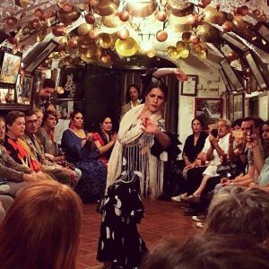 En una sala íntima y abarrotada con vasijas de cobre adornando el techo, una bailaora de flamenco actúa apasionadamente como en un Espectáculo de flamenco en la Zambra María la Canastera. - ForTwo - Planes para parejas