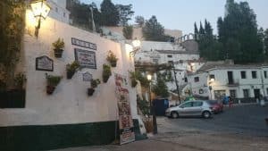 Un edificio blanco adornado con macetas de flores en la pared y un cartel de museo está situado en una encantadora calle bordeada de coches aparcados y árboles, que se hacen eco de los ritmos de espectáculos cercanos como el "Espectáculo de flamenco en la Zambra María la Canastera". - ForTwo - Planes para parejas
