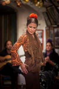 La bailaora de flamenco, con top estampado, mantón marrón y accesorios de pelo de color naranja vibrante, cautiva al público durante una intensa actuación que evoca el espíritu del "Espectáculo de flamenco en la Zambra María la Canastera". - ForTwo - Planes para parejas