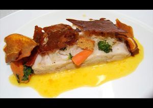 En el Restaurante El Vagón de Beni de Madrid, disfrute de un filete de pescado al plato con piel crujiente, acompañado de verduras frescas y una salsa amarilla vibrante. - ForTwo - Planes para parejas