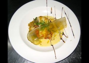 Un plato gourmet en el Restaurante El Vagón de Beni, un romántico lugar de temática ferroviaria en Madrid, ofrece carne perfectamente cocinada y hierbas vibrantes con una delicada rodaja de verduras y gotas de salsa artísticas en un plato blanco impecable. - ForTwo - Planes para parejas