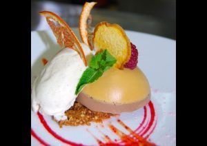 En el Restaurante El Vagón de Beni de Madrid, saborea un postre gourmet con helado, mousse cremosa, frambuesa, menta y frutos secos elegantemente colocados en un plato bellamente decorado. - ForTwo - Planes para parejas