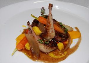 En Restaurante El Vagón de Beni - Un tren romántico en Madrid, disfrute de una codorniz asada con zanahorias y una rica salsa, elegantemente adornada con hierbas en un plato blanco, perfecto para una experiencia gastronómica romántica. - ForTwo - Planes para parejas