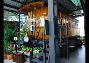 Restaurante El Vagón de Beni, un antiguo vagón de tren convertido en un romántico café en Madrid, está adornado con plantas en macetas y muebles de mimbre en un acogedor patio cubierto, y ofrece una mezcla de encanto histórico y encanto moderno. - ForTwo - Planes para parejas