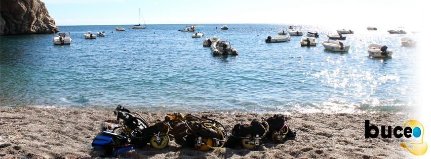 Playa de guijarros con equipo de buceo y embarcaciones ancladas en un mar en calma: una escapada de buceo ideal con "Paquete experiencia escapada de buceo en la costa de Granada. - ForTwo - Planes para parejas