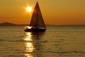 Un velero se recorta contra una puesta de sol, reflejándose en las aguas de Almuñécar, capturando la serena esencia de un tranquilo paseo romántico en barco en la Herradura y Almuñécar. - ForTwo - Planes para parejas