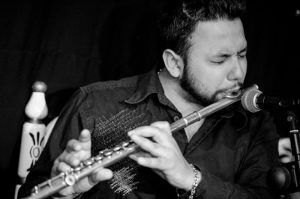 Un hombre toca la flauta con pasión, con los ojos cerrados, ante un micrófono frente a un fondo oscuro, evocando un Espectáculo de flamenco en los Jardines de Zoraya. - ForTwo - Planes para parejas