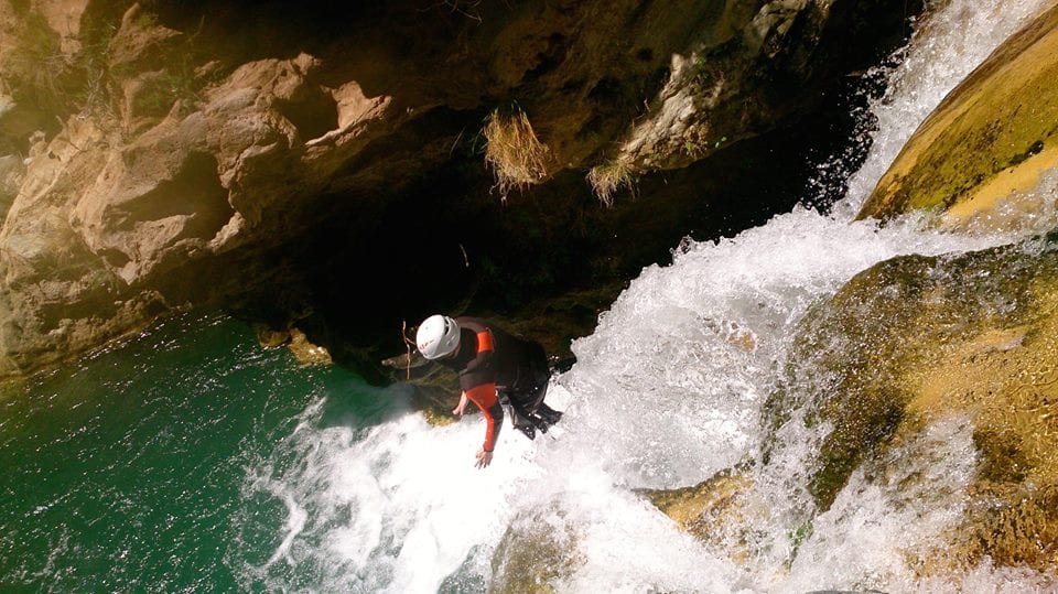 Un aventurero buscador de emociones, con casco, se sumerge en la refrescante piscina de la cascada durante la ruta completa de barranquismo de Río Verde, experimentando los impresionantes paisajes del Barranquismo en Granada. - ForTwo - Planes para parejas