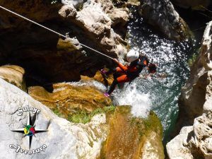 Un aventurero recorre el terreno rocoso de Río Verde, descendiendo con maestría por una cascada en el "Barranquismo en Granada - Ruta completa Río Verde". Ataviados con casco y traje de neopreno, se embarcan en la emocionante aventura del barranquismo, asegurados por una cuerda en medio de la majestuosidad de la naturaleza. - ForTwo - Planes para parejas