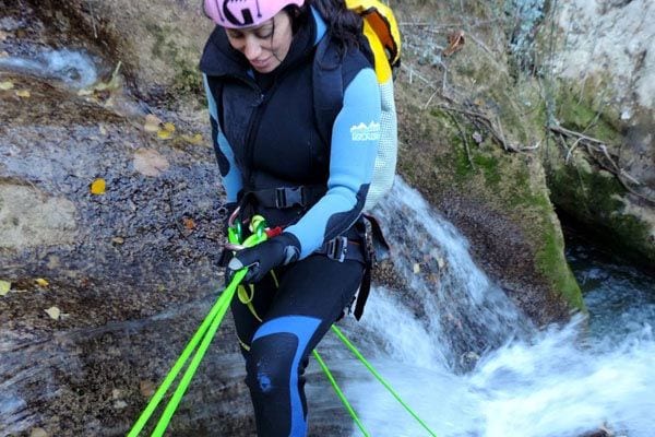 Vestido con traje de neopreno y casco, un aventurero utiliza cuerdas verdes vibrantes para descender en rapel por una cascada de Río Verde en Granada, mostrando el emocionante descenso de la experiencia Barranquismo en Granada - Ruta completa Río Verde. - ForTwo - Planes para parejas