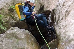 Con casco, traje de neopreno y mochila amarilla, un aventurero disfruta de un emocionante día de barranquismo mientras desciende en rapel por el cañón rocoso de Río Verde con la experiencia Barranquismo en Granada - Ruta completa Río Verde. - ForTwo - Planes para parejas