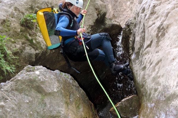 Con casco, traje de neopreno y mochila amarilla, un aventurero disfruta de un emocionante día de barranquismo mientras desciende en rapel por el cañón rocoso de Río Verde con la experiencia Barranquismo en Granada - Ruta completa Río Verde. - ForTwo - Planes para parejas