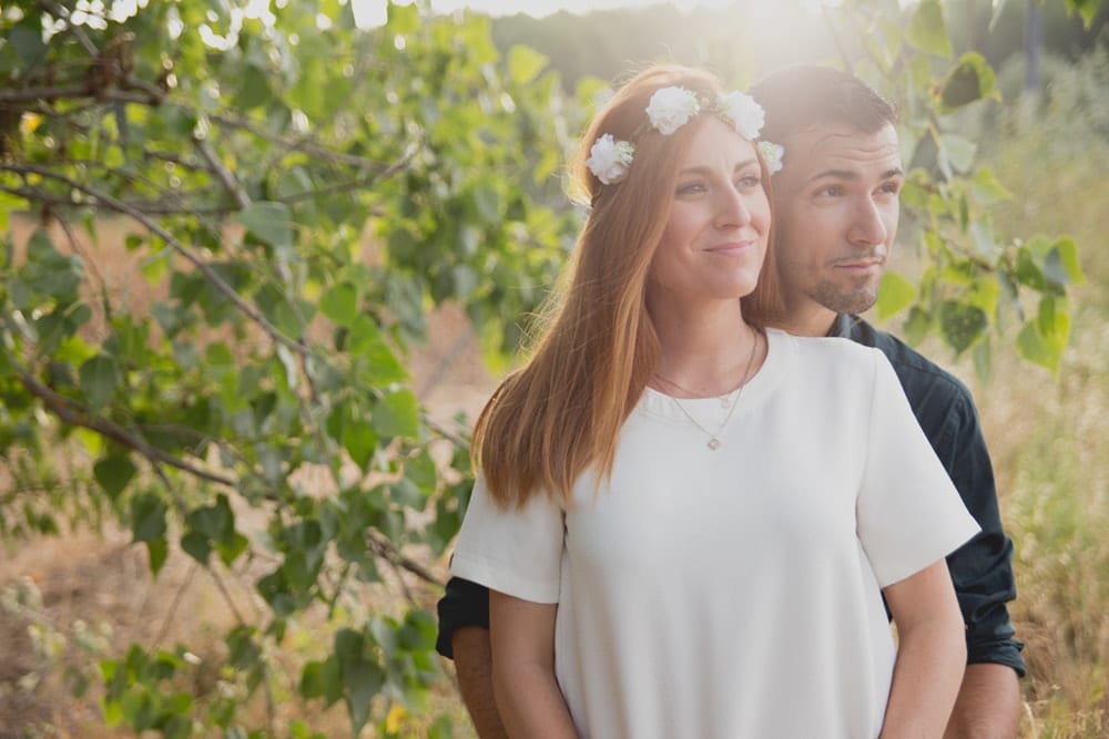 Una mujer con una corona de flores y un hombre están juntos en un entorno frondoso e iluminado por el sol durante su Sesión de fotografía en pareja por Carlos Fierro. - ForTwo - Planes para parejas