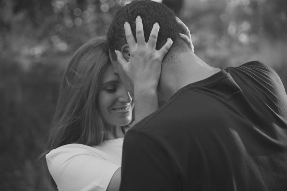 Una pareja se abraza estrechamente, sonriendo suavemente en un escenario al aire libre en blanco y negro, que recuerda a una "Sesión de fotografía en pareja por Carlos Fierro. - ForTwo - Planes para parejas