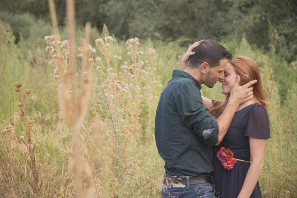 Una pareja abrazándose en un campo de hierba alta y flores silvestres captura la magia de una Sesión de fotografía en pareja de Carlos Fierro. - ForTwo - Planes para parejas