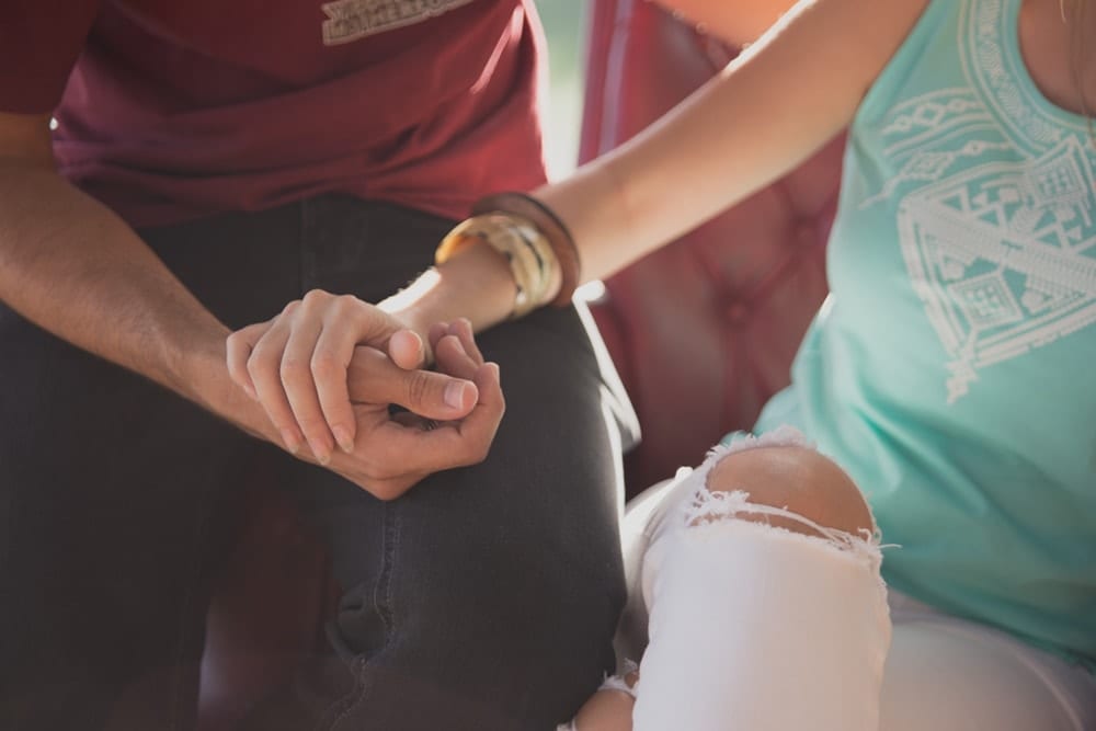 Tomada por Carlos Fierro durante una sesión de fotografía en pareja, esta imagen íntima muestra a una pareja tomada de la mano; una persona con una camisa marrón y la otra con un top turquesa con jeans blancos rotos. - ForTwo - Planes para parejas
