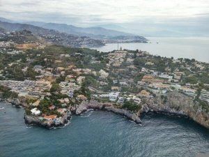 Vista aérea de la Costa Tropical, un pueblo costero de Granada con casas, acantilados rocosos y montañas distantes bajo un cielo nublado, como se ve desde un Vuelo en helicóptero por Costa Tropical Oeste de Granada. - ForTwo - Planes para parejas