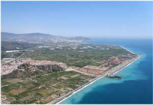 Una vista aérea de un pueblo costero con campos verdes, edificios y una playa de arena a lo largo de un mar azul brillante, capturada durante el "Vuelo en helicóptero sobre el Cañón Tajo de los Vados. - ForTwo - Planes para parejas