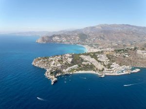 Una vista aérea muestra una ciudad costera llena de vegetación y edificios, enmarcada por montañas y el mar, que recuerda las impresionantes vistas desde un vuelo en helicóptero sobre el Cañón Tajo de los Vados. - ForTwo - Planes para parejas