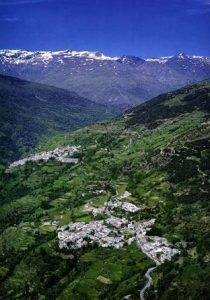 Vista aérea de pequeños pueblos enclavados en las exuberantes montañas verdes con Vuelo en helicóptero sobre el sur de Granada, mostrando picos nevados bajo un cielo despejado. - ForTwo - Planes para parejas