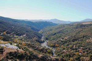 Vista aérea de un exuberante valle de Granada con un río sinuoso, enmarcado por colinas y montañas bajo un cielo despejado, como si se experimentara durante el sereno "Vuelo en helicóptero sobre el sur de Granada". - ForTwo - Planes para parejas