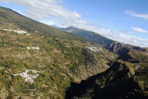 El vuelo en helicóptero sobre el sur de Granada ofrece una vista aérea de su paisaje montañoso, con edificios blancos dispersos y parches de vegetación bajo un cielo parcialmente nublado. - ForTwo - Planes para parejas