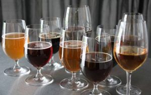 Una selección de vasos llenos de cerveza reposa elegantemente sobre una superficie metálica, frente a un fondo de cortina gris, evocando la sofisticada experiencia del "Taller de cata y degustación de cerveza en Barcelona". - ForTwo - Planes para parejas