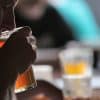 En un ambiente tenue, alguien saborea los ricos sabores de un Taller de cata y degustación de cerveza en Barcelona. Las copas chocan suavemente mientras las figuras borrosas al fondo realzan esta íntima experiencia de cata de cerveza. - ForTwo - Planes para parejas