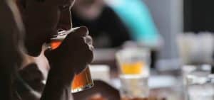 En un ambiente tenue, alguien saborea los ricos sabores de un Taller de cata y degustación de cerveza en Barcelona. Las copas chocan suavemente mientras las figuras borrosas al fondo realzan esta íntima experiencia de cata de cerveza. - ForTwo - Planes para parejas