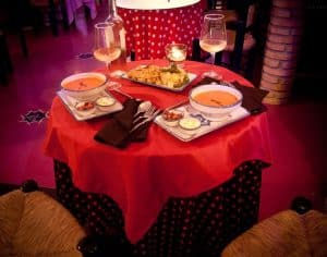 Disfrute de una acogedora experiencia gastronómica con el Menú Tapeo, que incluye sopa, aperitivos y vino, servido sobre un mantel de lunares rojos en una habitación oscura que recuerda a El Templo del Flamenco. - ForTwo - Planes para parejas