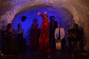 En el famoso El Templo del Flamenco, una bailarina de rojo electrifica el escenario con un espectáculo, rodeada de músicos en medio de un telón de fondo similar a una cueva. - ForTwo - Planes para parejas