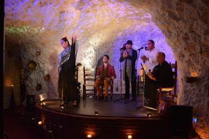 En El Templo del Flamenco, el "Espectáculo + Menú tapeo" presenta a una cautivadora bailaora de flamenco en el escenario de la cueva, con músicos tocando la guitarra y aplaudiendo rítmicamente. - ForTwo - Planes para parejas
