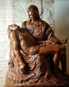 Una impresionante escultura de chocolate representa una escena de la Piedad con una figura sentada acunando a otra, elaborada por maestros del chocolate en el renombrado Museo de la Xocolata como parte de la inolvidable "Descubre la Xocoexperiencia en el Museo de la Xocolata y podréis convertiros en maestros del chocolate. - ForTwo - Planes para parejas