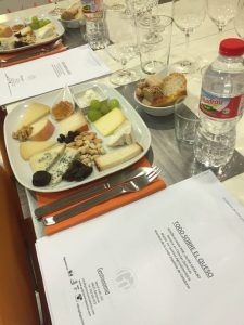 Una mesa elegantemente puesta ofrece platos con quesos, frutos secos, fruta y pan. Copas de vino y botellas de agua realzan esta deliciosa experiencia de "Taller de cata y degustación de quesos artesanos en Barcelona". - ForTwo - Planes para parejas