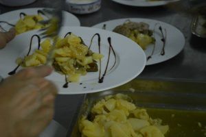 En una cocina, alguien está preparando de forma creativa una ensalada de patatas con glaseado balsámico, que recuerda al vibrante tapeo Espectáculo + Menú de El Templo del Flamenco. - ForTwo - Planes para parejas