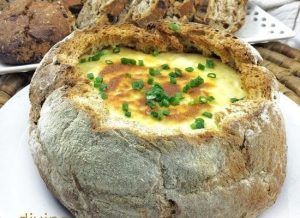 Este cuenco de pan redondo relleno de queso horneado y cubierto con cebollas verdes ofrece una deliciosa pieza central para cualquier "Taller de cata y degustación de quesos artesanos en Barcelona", con rebanadas de pan en el fondo para una experiencia de degustación artesanal completa. - ForTwo - Planes para parejas