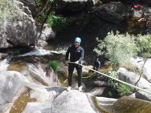 Con casco, una persona desciende en rápel por una cascada rocosa entre una exuberante vegetación, capturando la emoción del Pack multiaventura en pareja en Madrid. - ForTwo - Planes para parejas