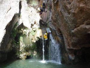 Durante la Pack multiaventura en pareja en Madrid, alguien desciende en rápel por la cascada de un cañón rocoso mientras su pareja y otras personas esperan ansiosamente arriba. - ForTwo - Planes para parejas