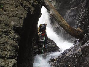 En el "Pack multiaventura en pareja en Madrid", un aventurero desciende en rápel por una cascada enclavada entre acantilados rocosos, con el tronco de un árbol sobre su cabeza. - ForTwo - Planes para parejas